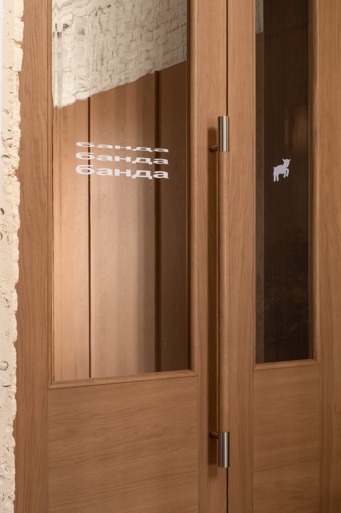 Oak entrance door with banda repeated in white lettering on the glazed panel and a small goat emblem