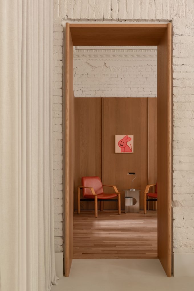 View through an oak-lined doorway to red vintage armchairs and a naive painting of a pink rabbit, white-painted brick around