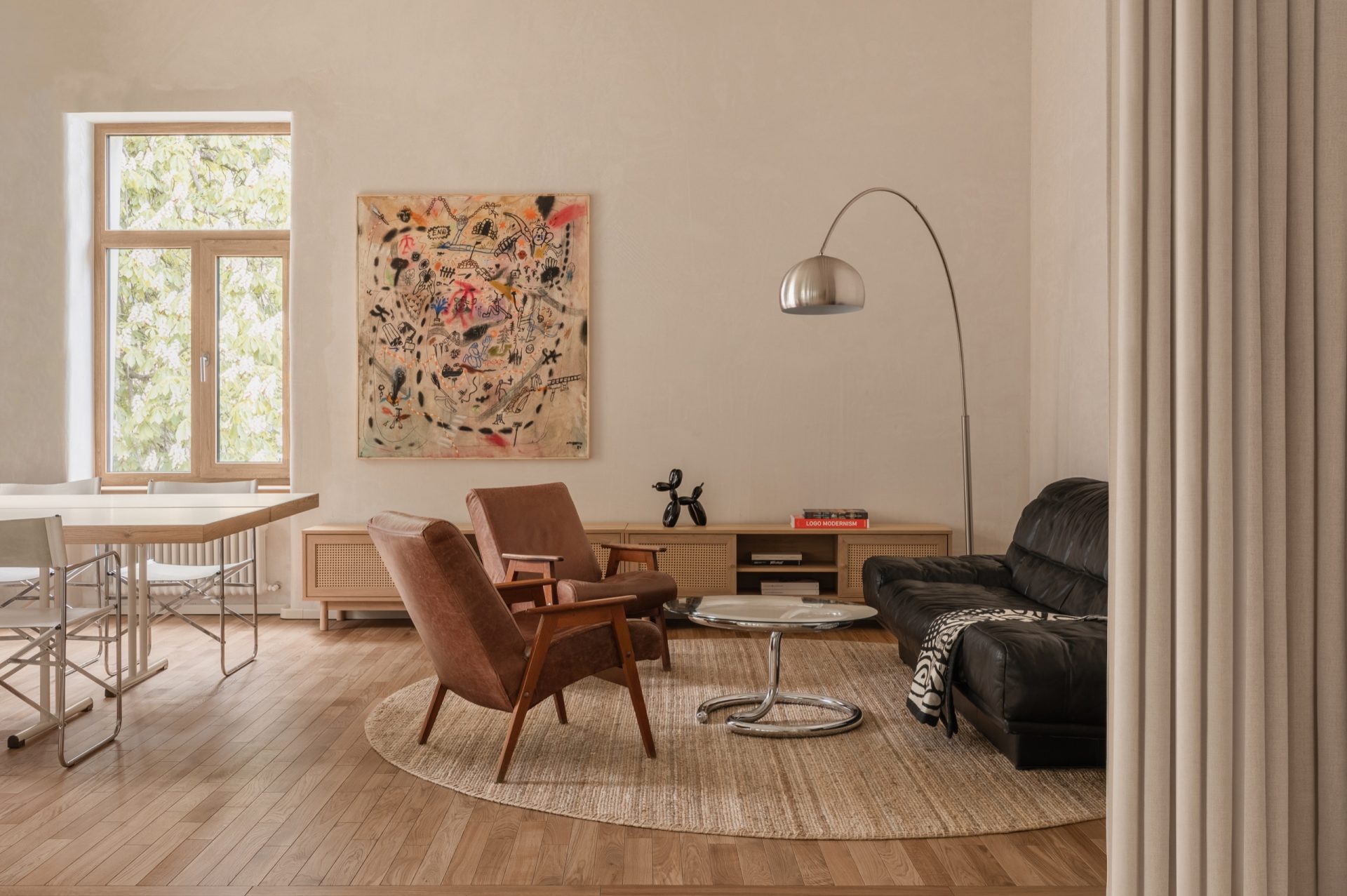 Lounge with brown velvet armchairs, a cane-fronted credenza and black leather sofa beneath a large abstract painting