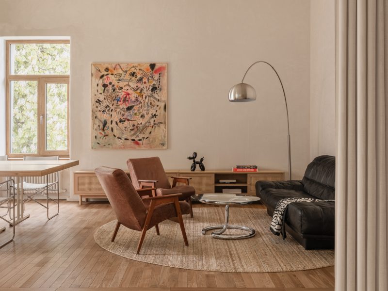 Lounge with brown velvet armchairs, a cane-fronted credenza and black leather sofa beneath a large abstract painting