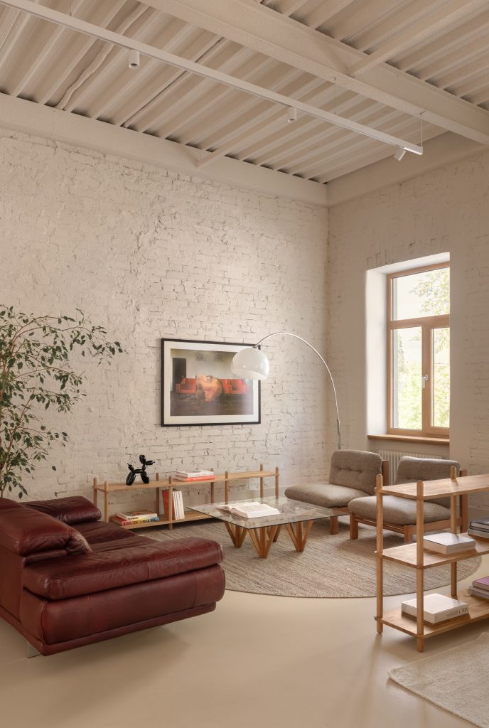 Oxblood leather sofa, glass coffee table and a balloon-dog sculpture against whitewashed brick, a ficus alongside