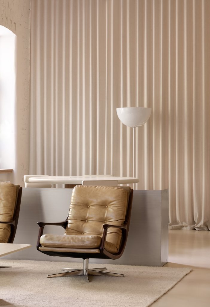 Vintage tan leather swivel chairs and a stainless counter in front of a full-height curtain, an uplighter beside