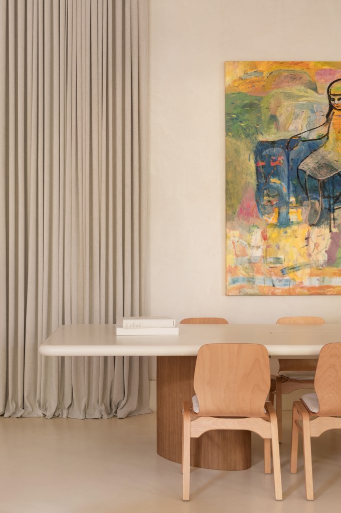 Cream meeting table with bentwood chairs before a large colourful figurative painting, curtain to one side