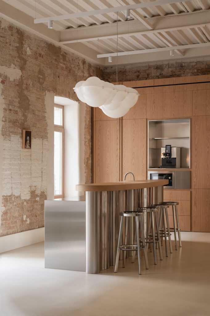 Kitchen island with a fluted stainless base and oak top, chrome stools, oak cabinetry and a Nuvola cloud pendant above