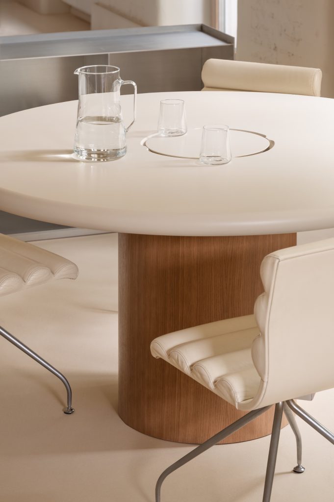 Detail of a round cream table on an oak drum base with cream leather swivel chairs