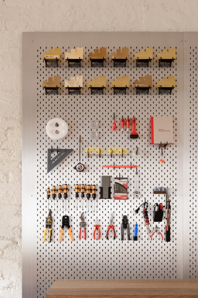 Close view of the pegboard: rows of miniature chairs above pliers, screwdrivers and set squares