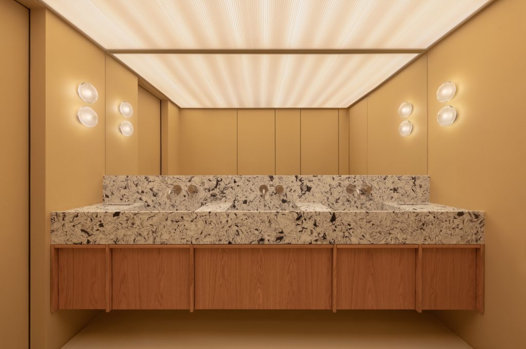 Ochre-lined washroom with a speckled quartzite trough counter, round glass sconces and a mirrored ceiling