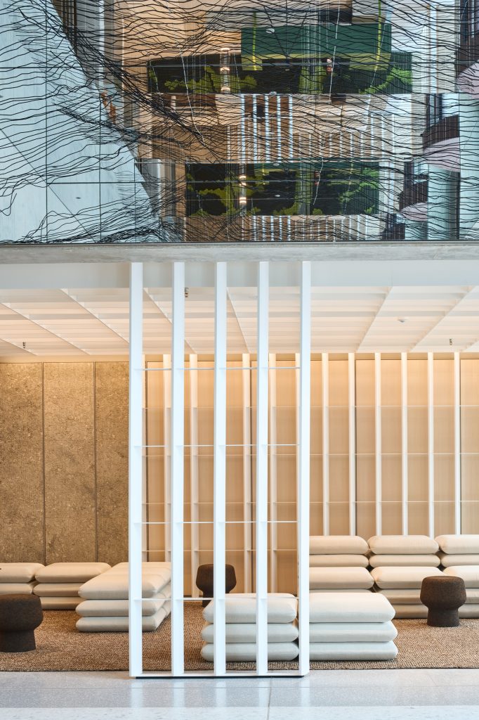 Lounge of stacked cushion seating beneath a suspended wire installation and mirrored ceiling, cork stools between