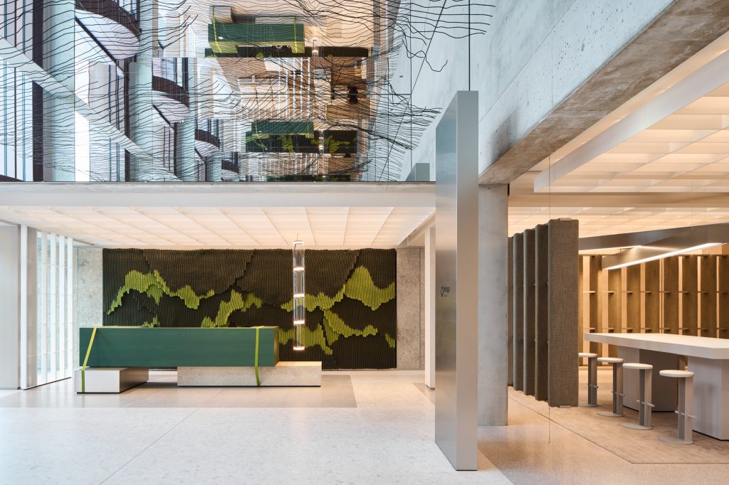 Lobby with a green reception desk strapped like a shipping crate, a woven rope artwork behind and the wire wave mirrored above