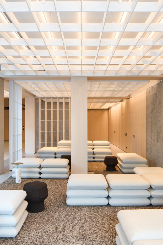 Cushion-stack seating groups with cork stools beneath a luminous coffered ceiling