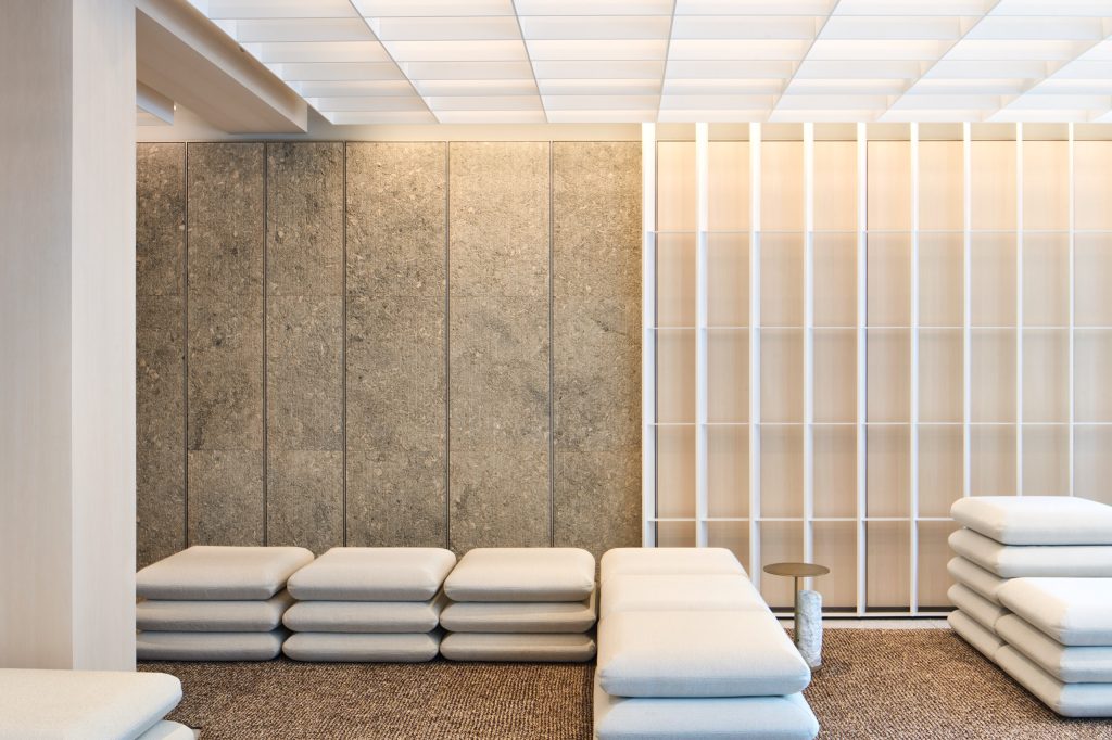 Cushion benches along a shell-limestone wall, a white shelving grid filtering the light