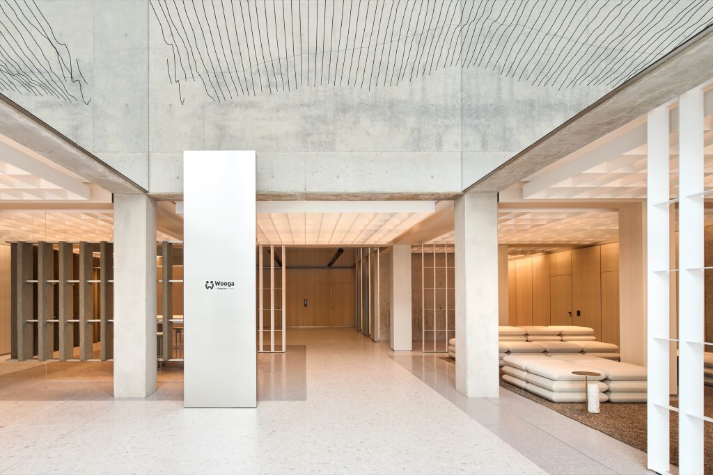 Second lobby with a white tenant pylon between concrete columns, cushion lounges and the mirrored band above