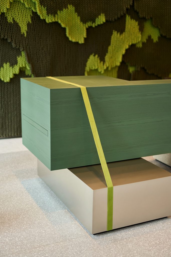 Green ash reception desk cinched with a lime strap, the knitted rope artwork rising behind