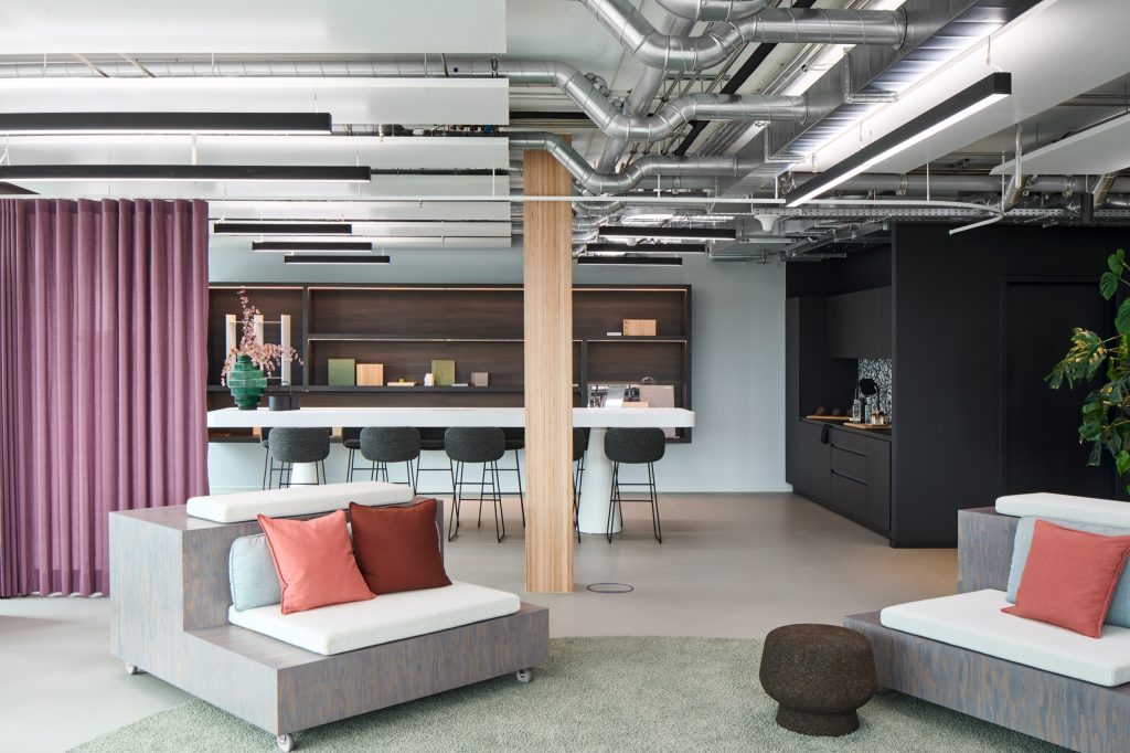Suite seen past the sample bar: white island with stools, black kitchen, plum curtain and exposed ductwork