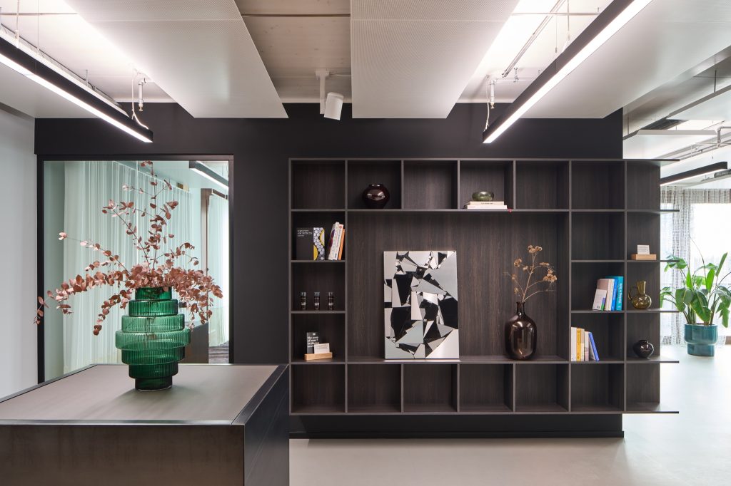 Dark shelving with material samples and a mirror-mosaic artwork, a ribbed green vase on the steel counter