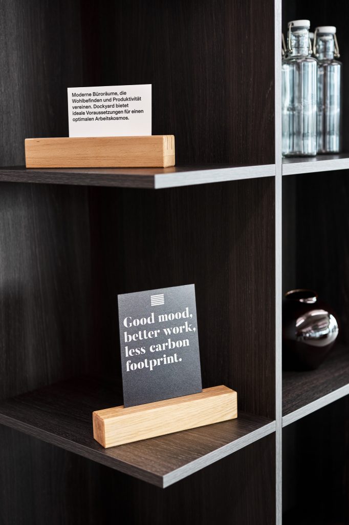 Postcards in oak stands on dark shelving, one reading good mood, better work, less carbon footprint