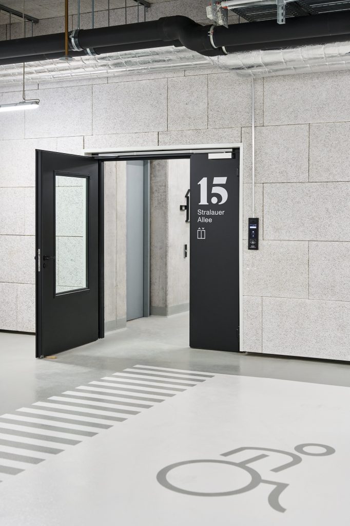 Parking-level door marked 15 Stralauer Allee, zebra and wheelchair markings painted on the pale floor