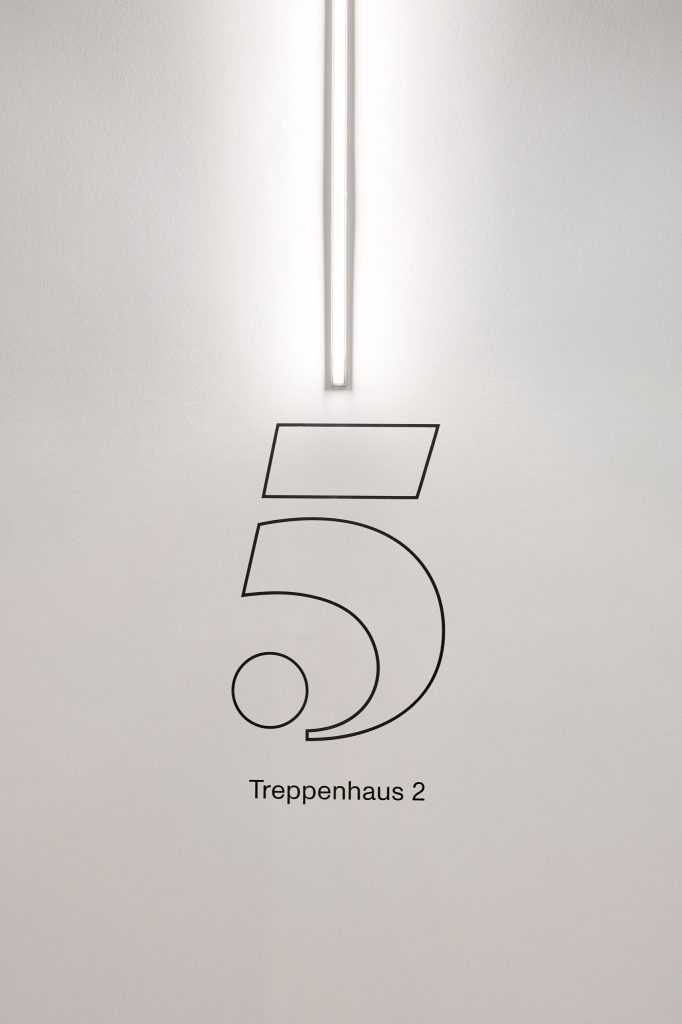 Painted outline numeral five above the words Treppenhaus 2, lit by a vertical wall light