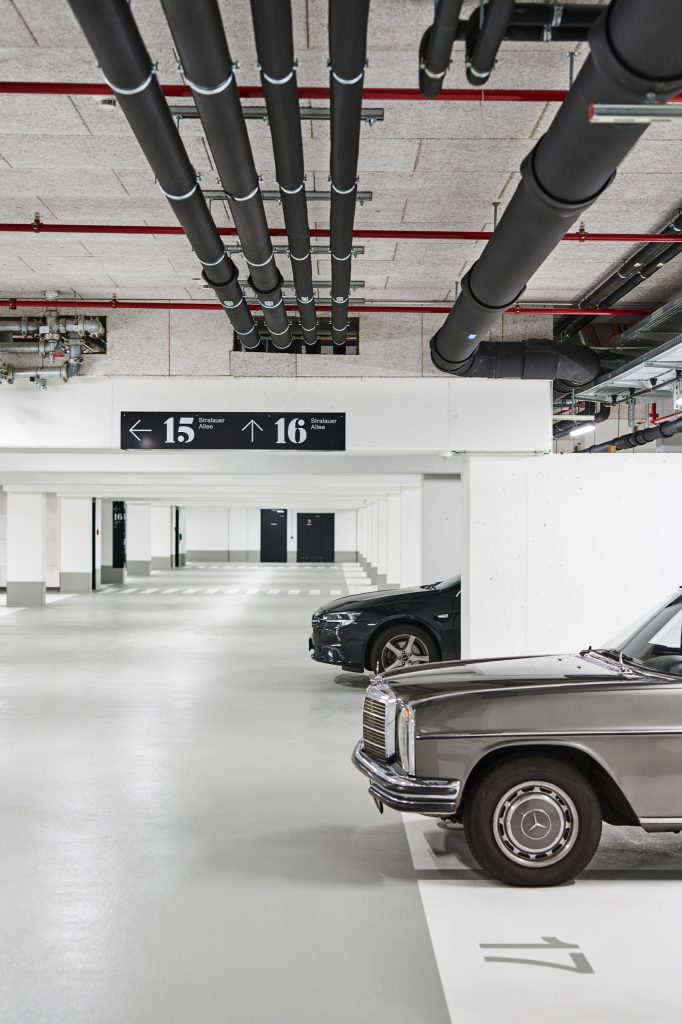 Directional sign for buildings 15 and 16 hung among the garage's insulated pipework, a vintage Mercedes parked below
