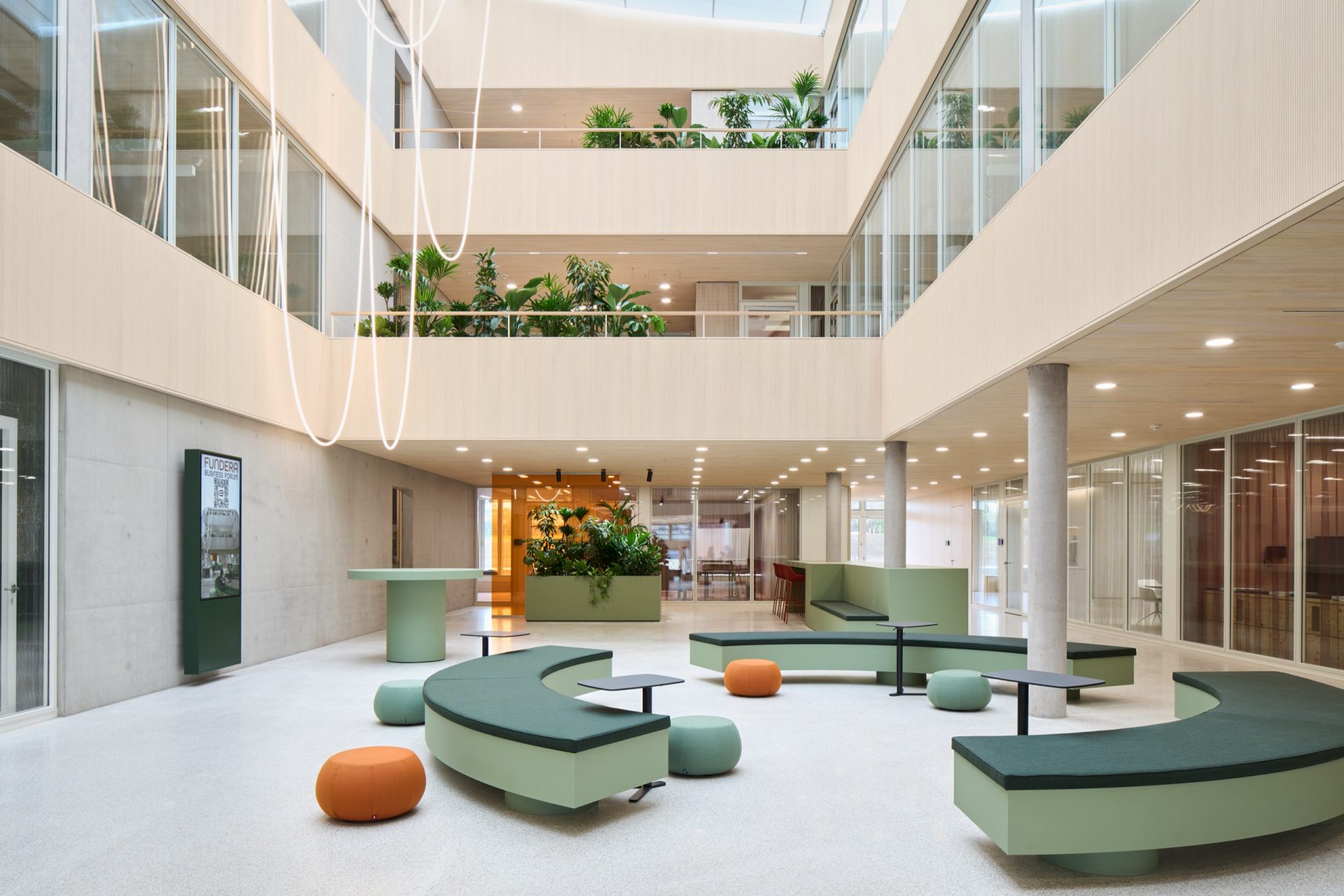 Atrium floor with curved green benches, orange poufs and a tubular light sculpture hanging through three planted storeys