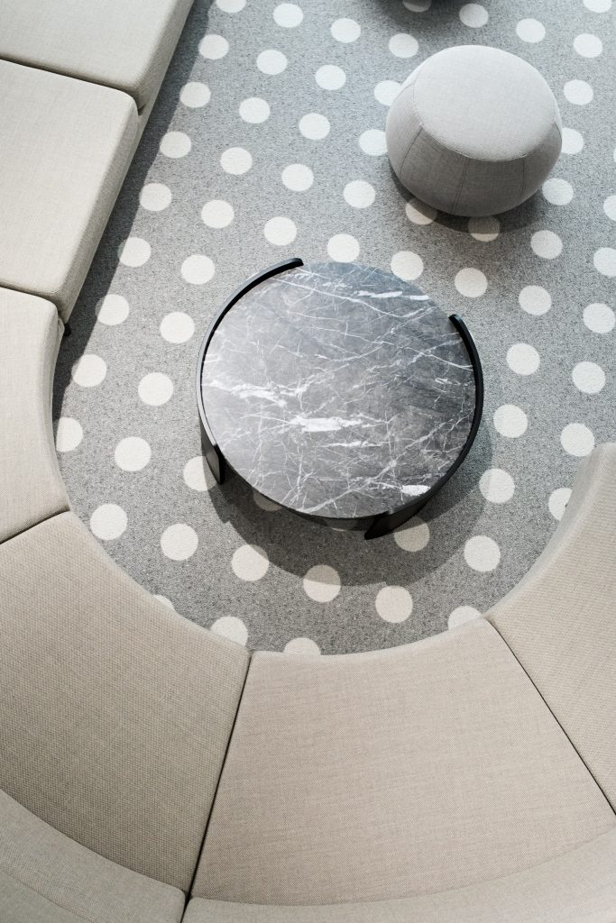 Overhead view of a circular beige banquette around a grey marble table on dotted carpet