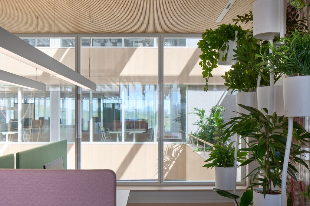 Balcony seating in green and pink beside a wall of white planters, looking across the atrium to workspaces