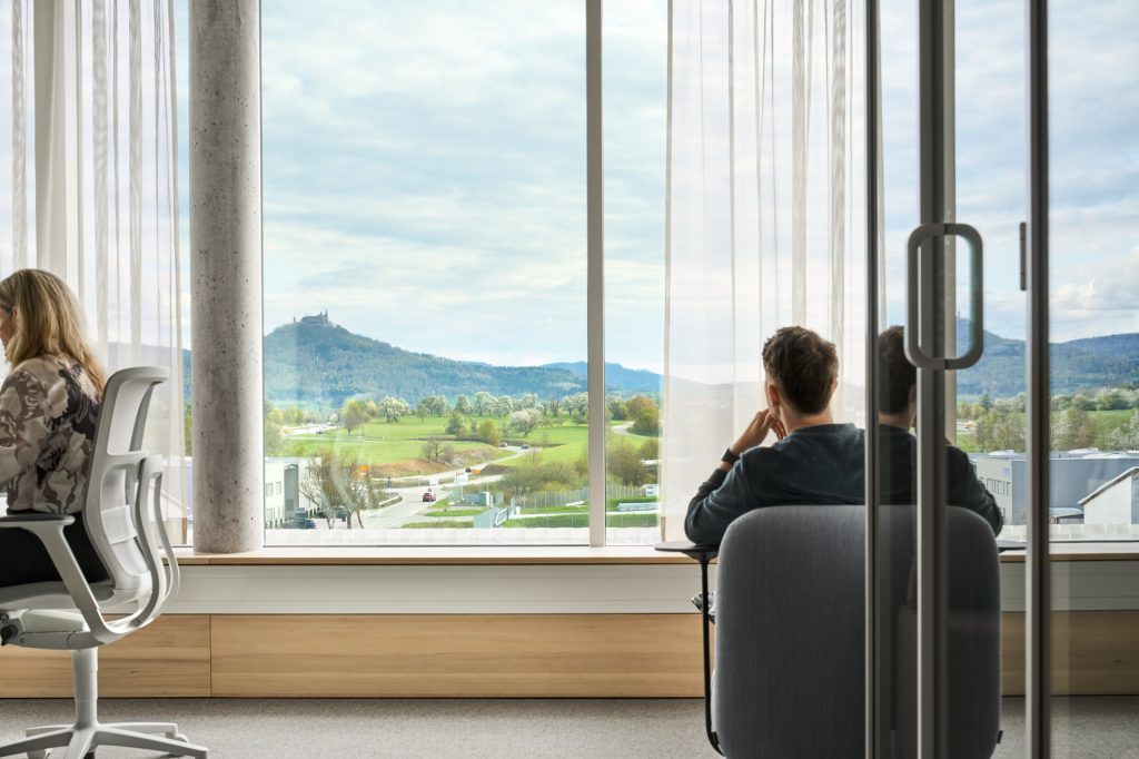 Two people at a window bench looking out across meadows to Hohenzollern Castle on its wooded hill