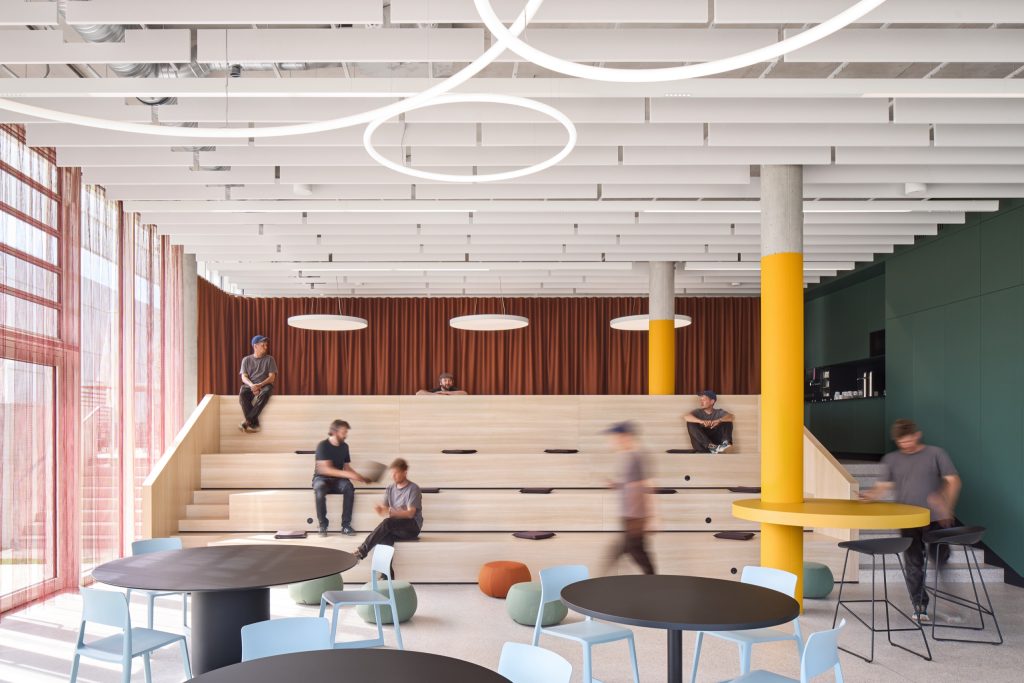 Restaurant with a stepped timber seating terrace, people sitting on the treads, a rust curtain behind and ring pendants above