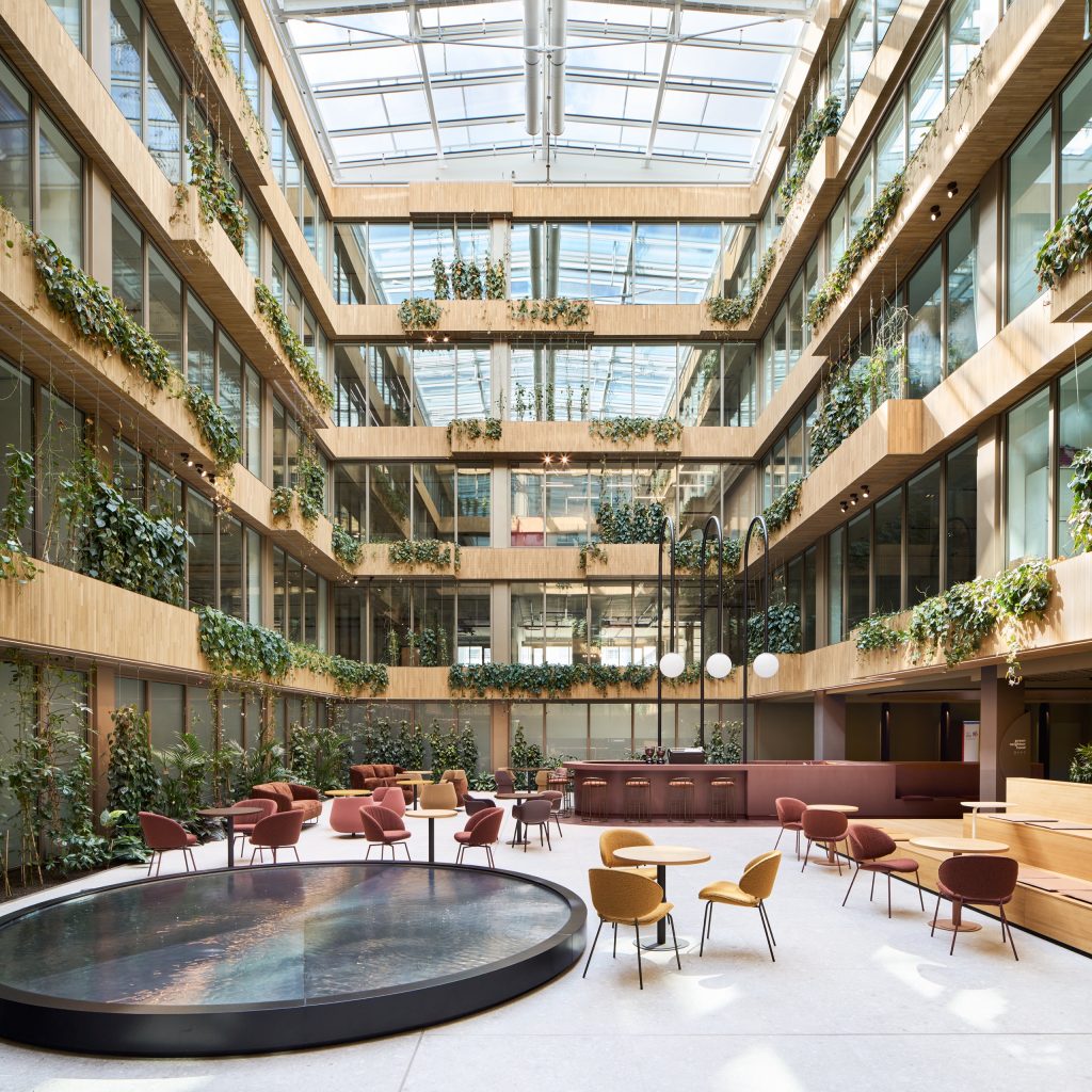 Four-storey atrium with planted balconies under a glass roof, a circular water table and cafe seating below