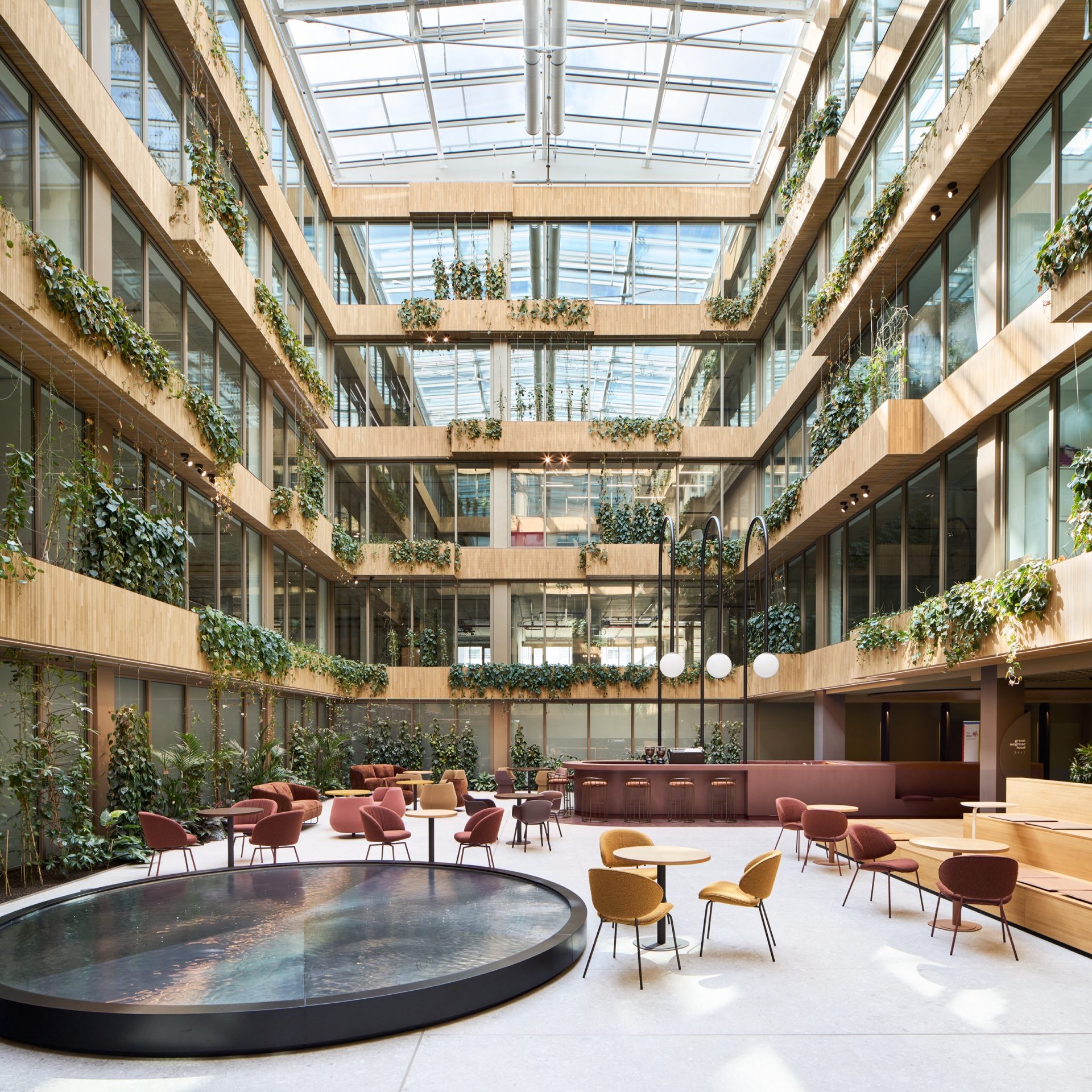 Four-storey atrium with planted balconies under a glass roof, a circular water table and cafe seating below