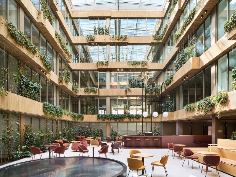 Four-storey atrium with planted balconies under a glass roof, a circular water table and cafe seating below