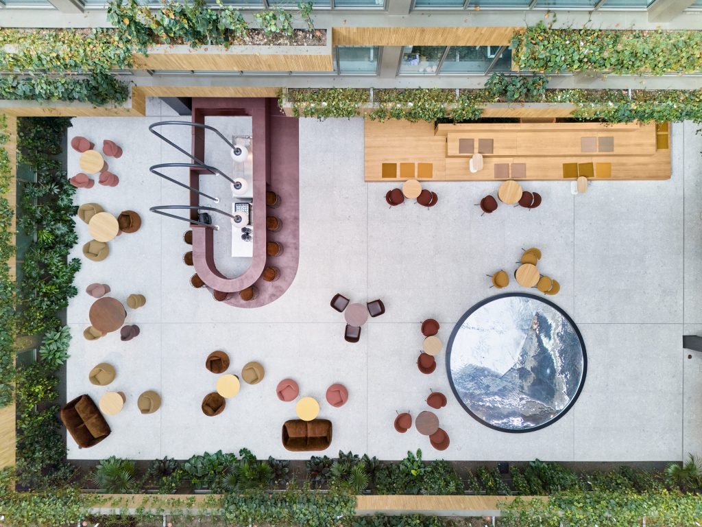 The atrium floor from above: the oxblood cafe bar, tiered timber platform and circular water table among lounge seating