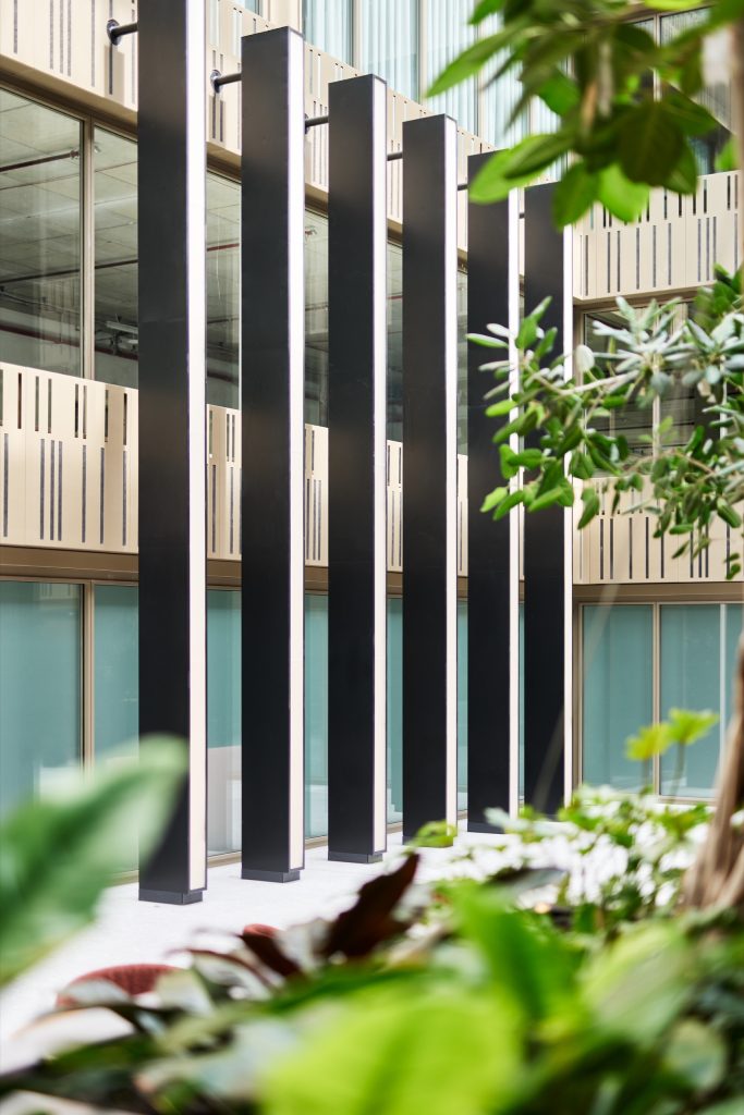 Black columns with luminous edges rising among planting, perforated parapet panels behind