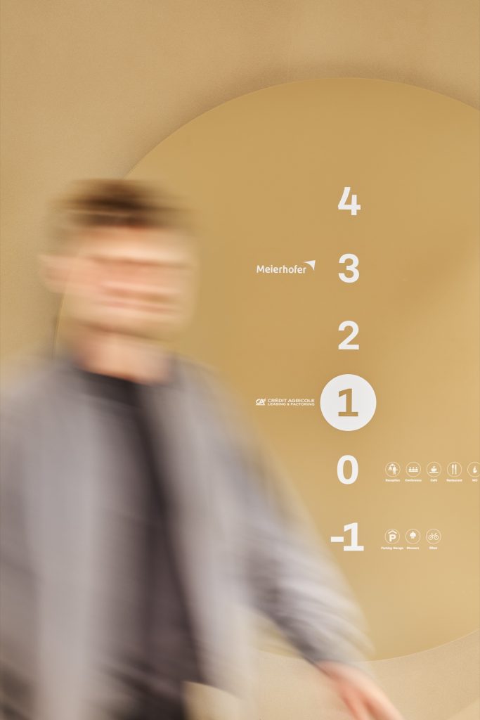 Floor directory on an ochre disc listing the campus tenants, a person passing in motion blur