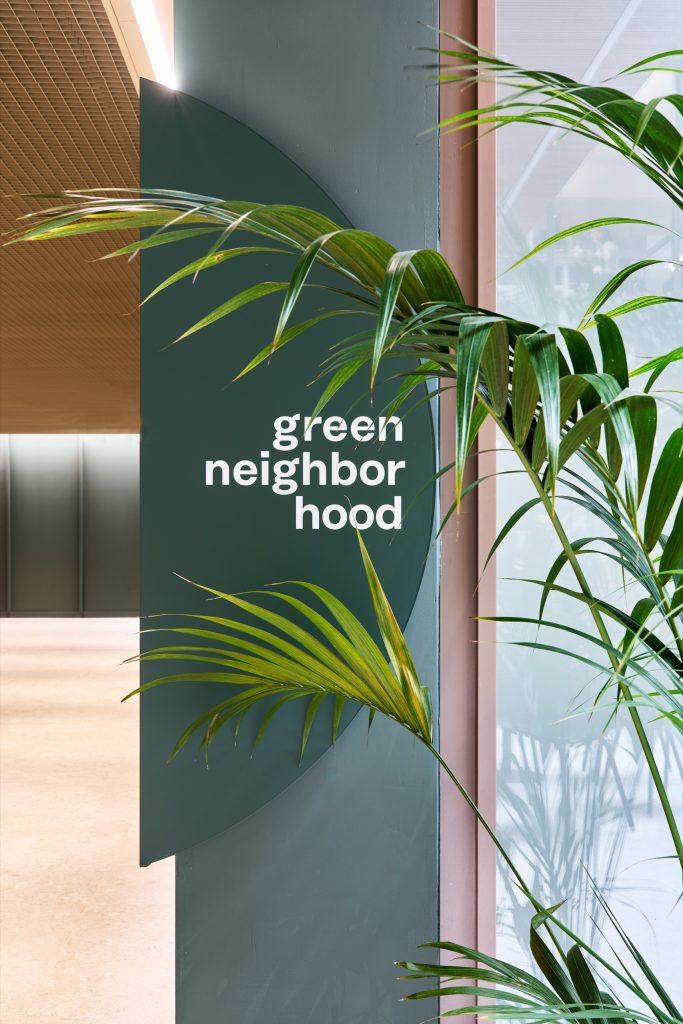 Deep-green wayfinding disc reading green neighbourhood, palm fronds crossing it