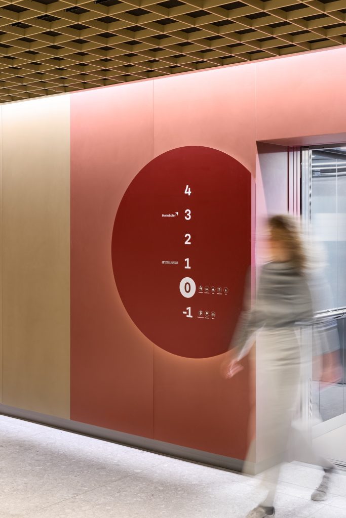 Floor directory on a deep-red disc beside the lift, tenants listed floor by floor