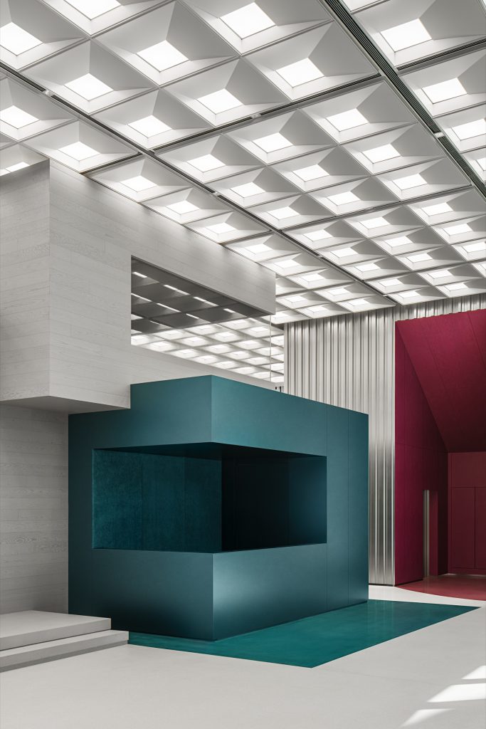 Teal reception counter beneath a coffered luminous ceiling, with a deep-red auditorium volume beyond
