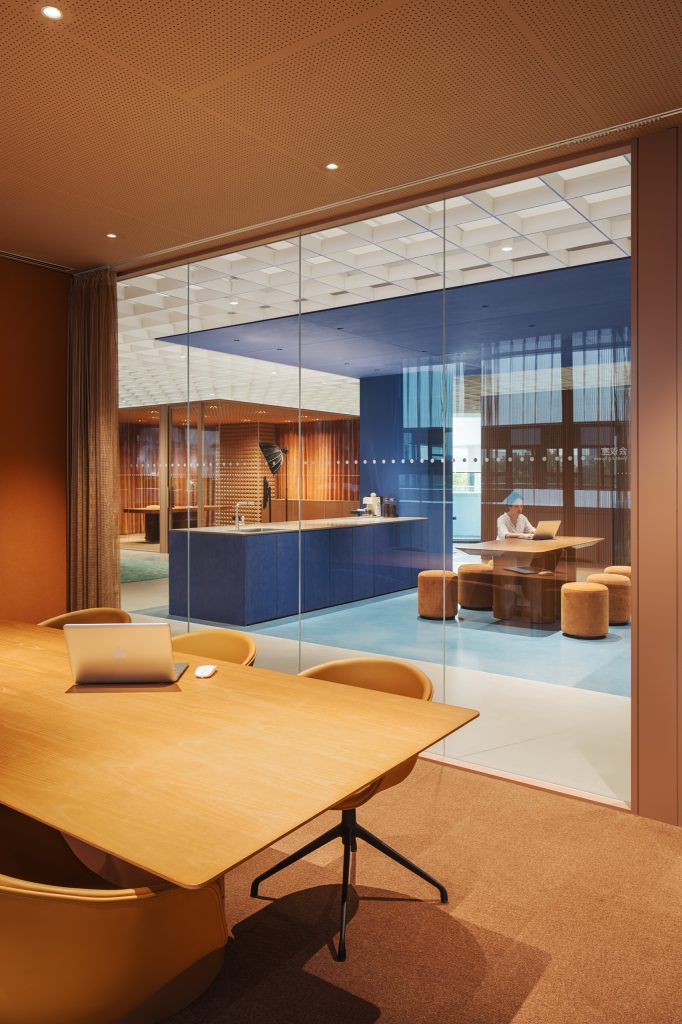 Terracotta meeting room looking through glass to a blue pantry island and touchdown tables
