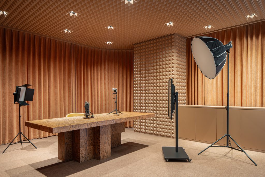 Broadcast studio lined with pyramid acoustic foam and velvet curtains, softbox lights around a timber table
