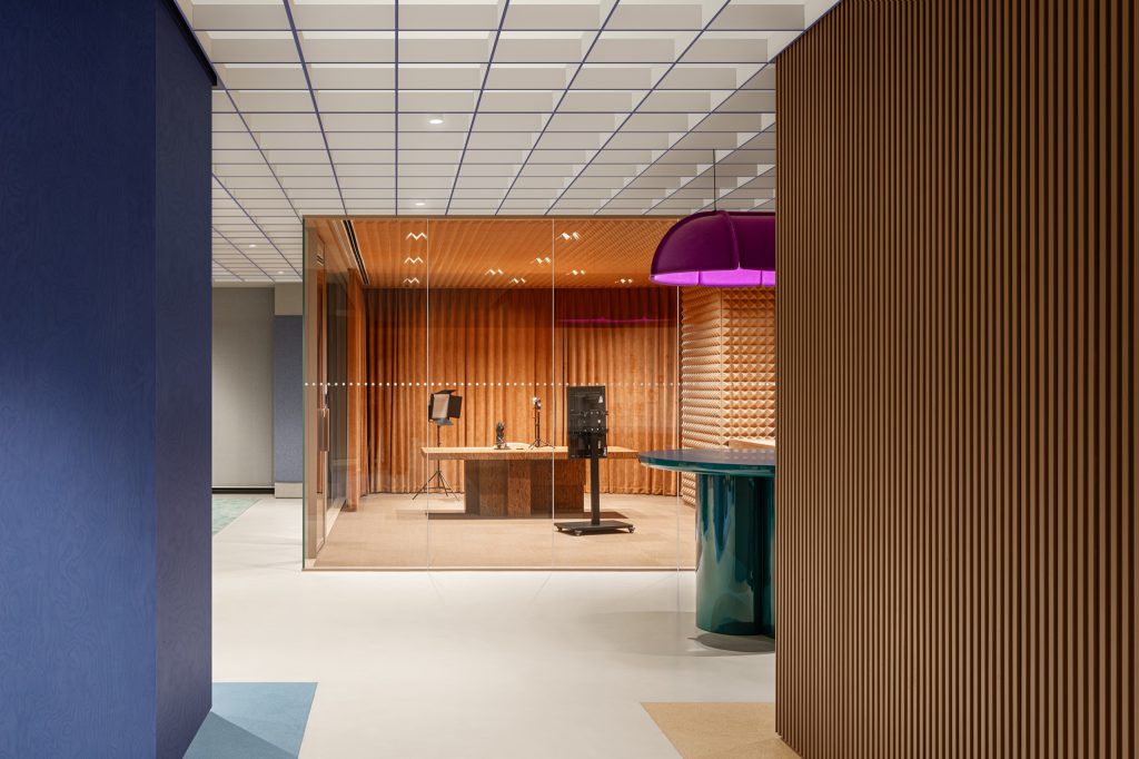 View past a fluted timber drum and purple felt pendant into the glass-walled broadcast studio