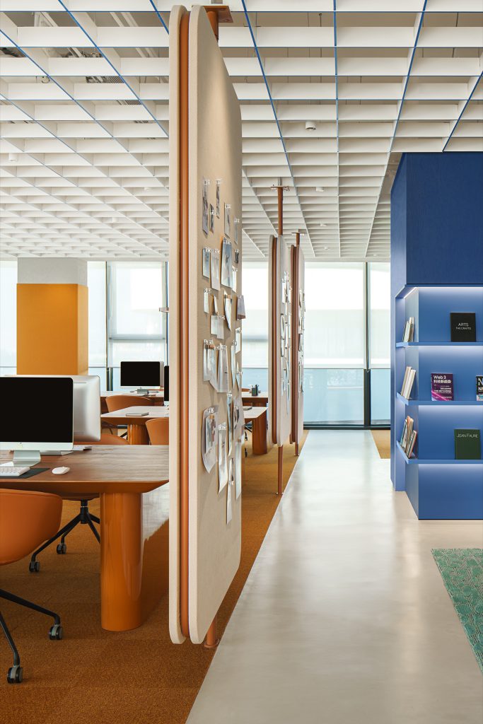 Open workspace with timber desks, tan leather chairs and suspended pin-board screens, books displayed in blue joinery