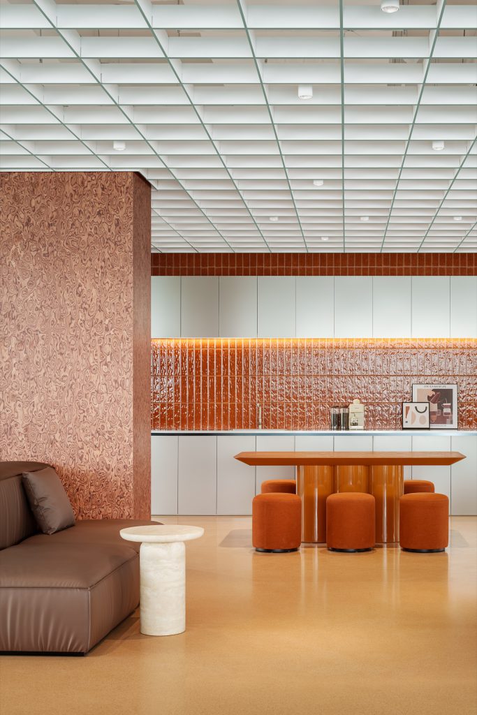 Tea point with amber glass-tiled splashback, lacquered orange table and terracotta poufs beside a leather sofa