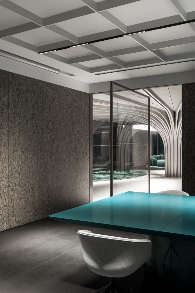 Meeting room with teal table and smoked-veneer walls, looking out to the tree-column lobby