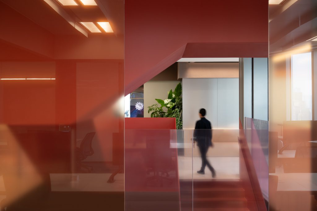 Stair landing seen through colour-tinted glass, with planting and workspaces beyond