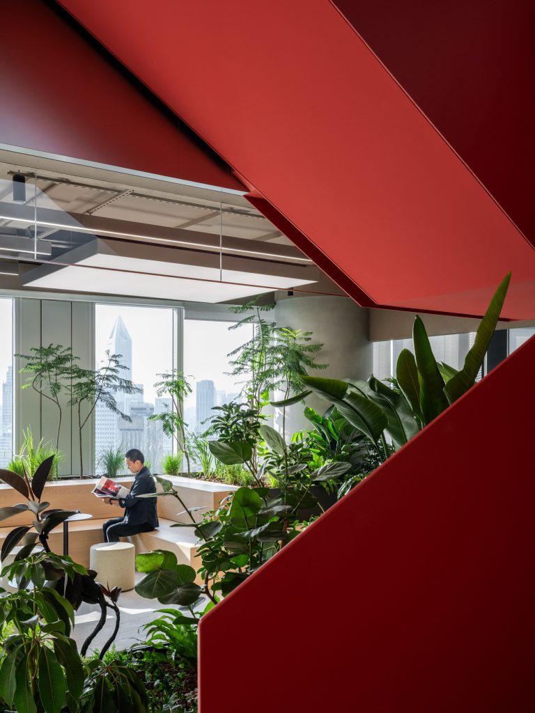 Tiered timber courtyard seating wrapped in dense planting beside the red staircase, the Shanghai skyline beyond