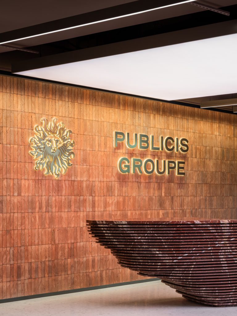 Reception with a red ceramic brick wall, backlit Publicis Groupe lion emblem and a layered dark-red stone desk