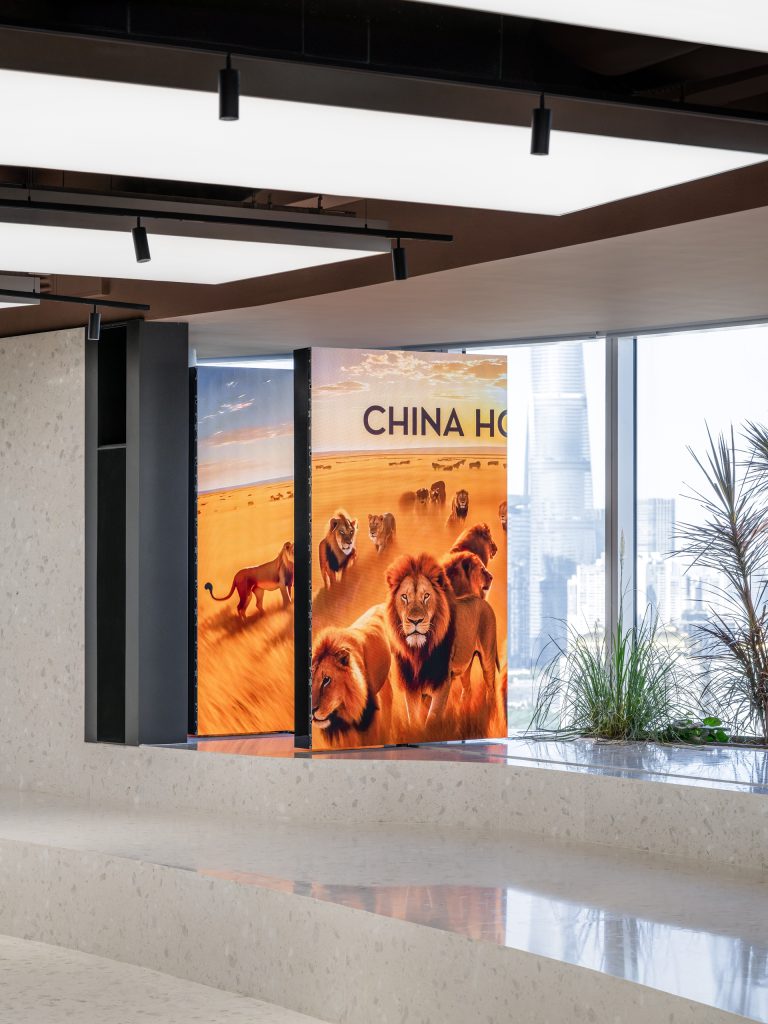 Movable LED screens showing lion artwork beside window planting, the Shanghai skyline beyond