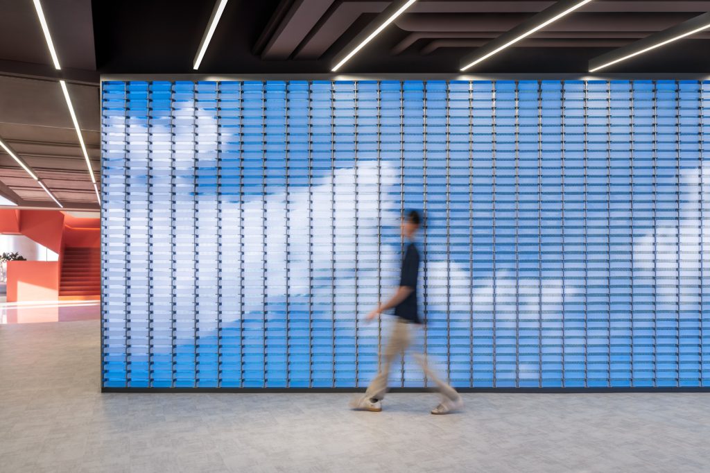 A wall of LED-embedded glass bricks displaying a sky animation, beside the red staircase