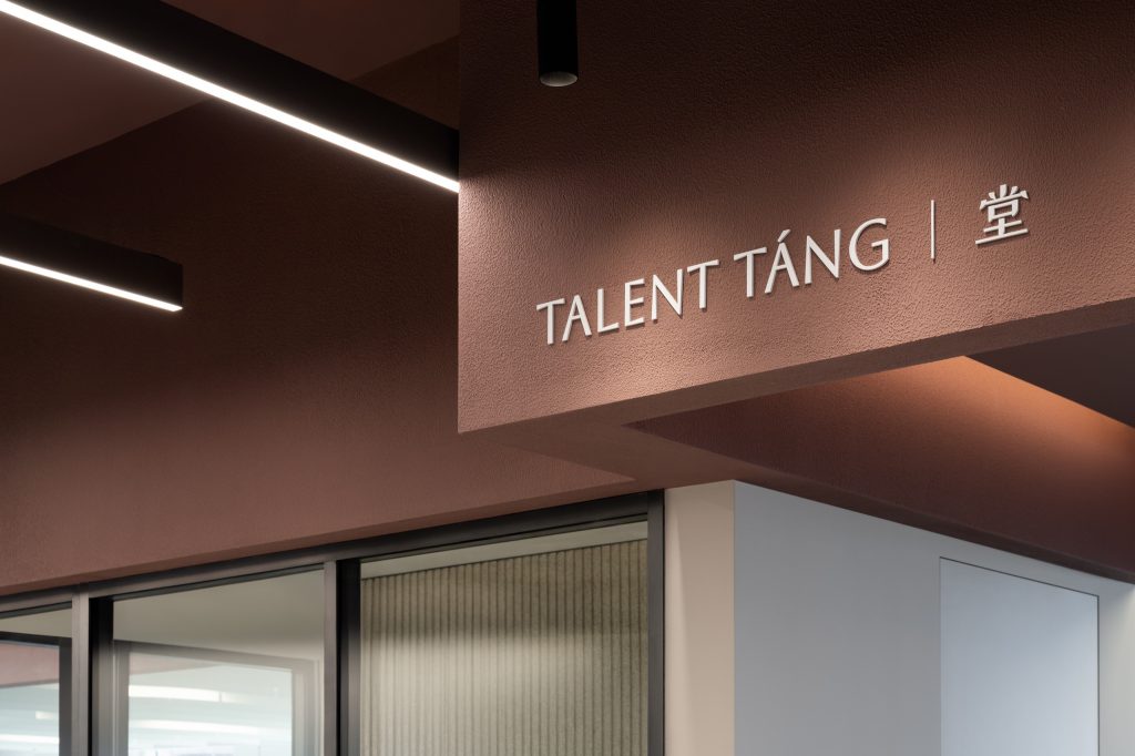 White lettering reading Talent Tang on a terracotta wall above a glass-walled meeting room