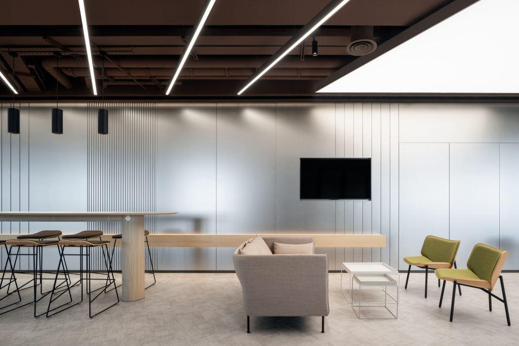 Lounge seating against the stainless-steel core, a continuous timber shelf running its length
